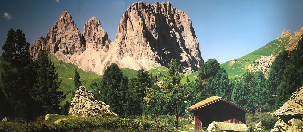 Wandbild einer Bergkulisse mit Almhütte als raumhohe Fototapete