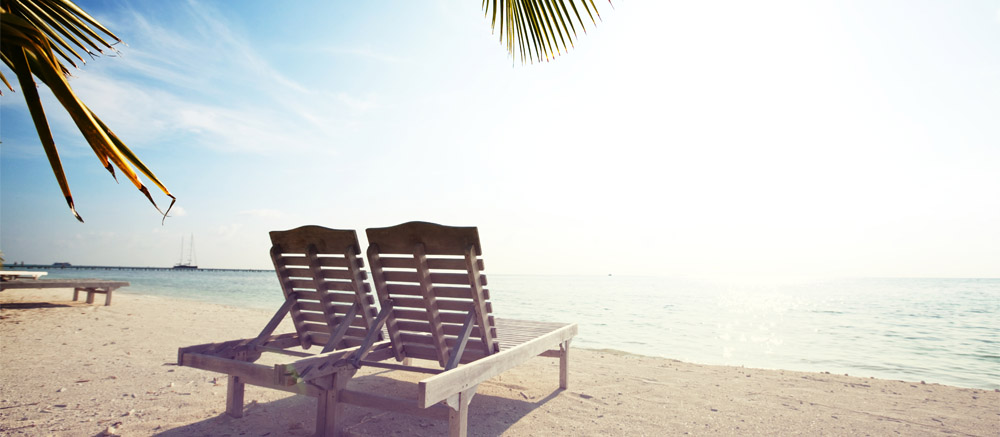 Zwei Liegestühle am Strand unter Palmen – Sinnbild für den Urlaubsservice